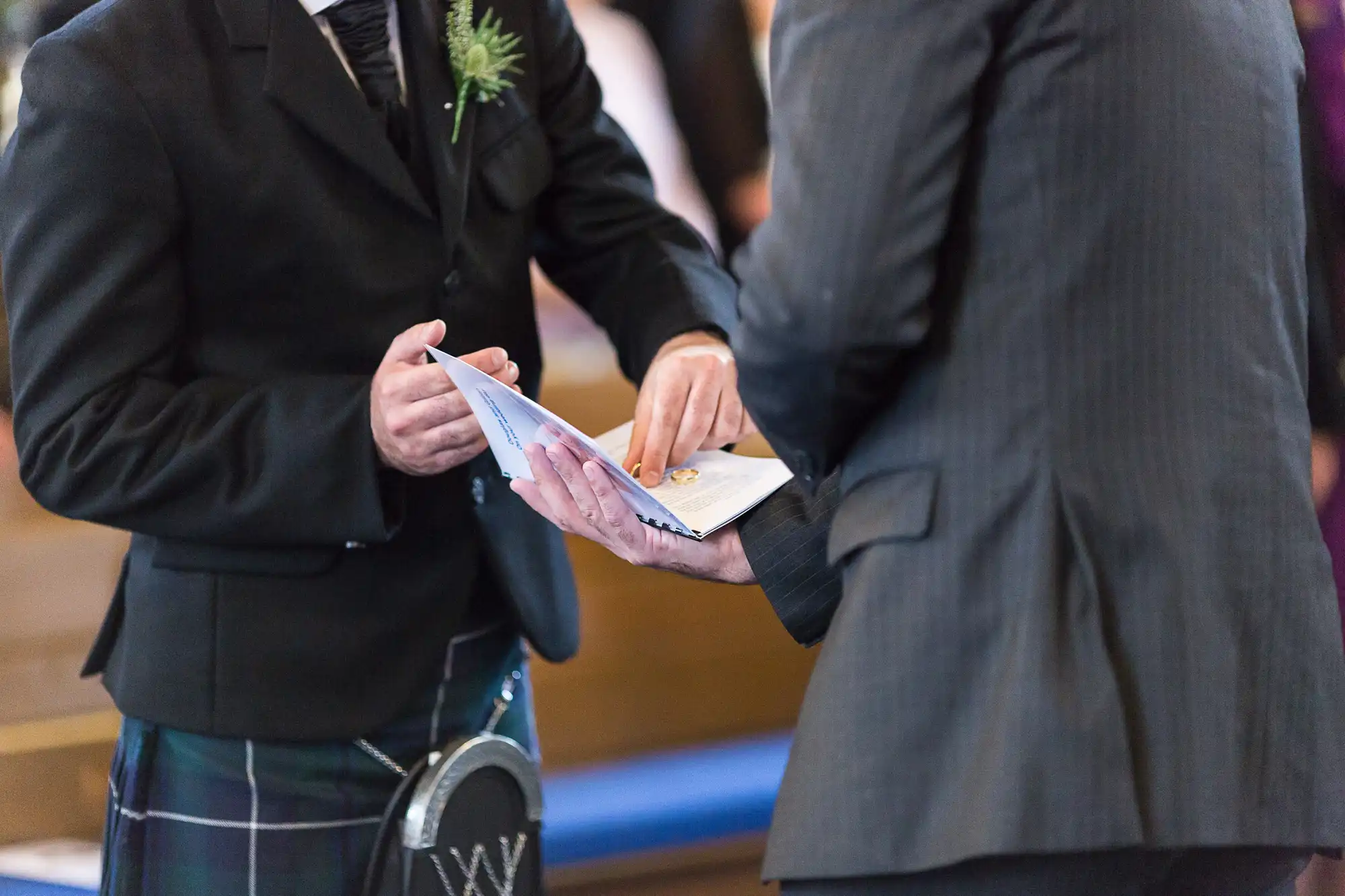 Two men exchanging wedding rings and vows, one wearing a kilt, during a ceremony indoors.