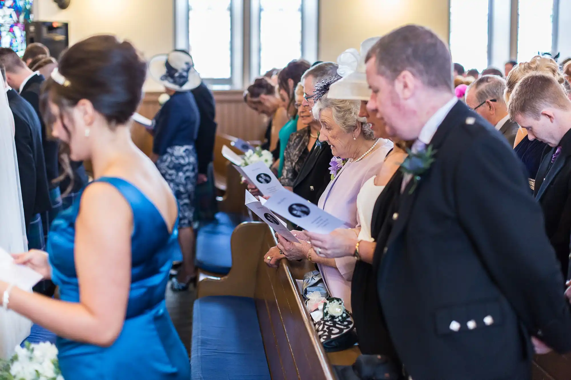 Guests in formal attire reading programs inside a church during a wedding ceremony.