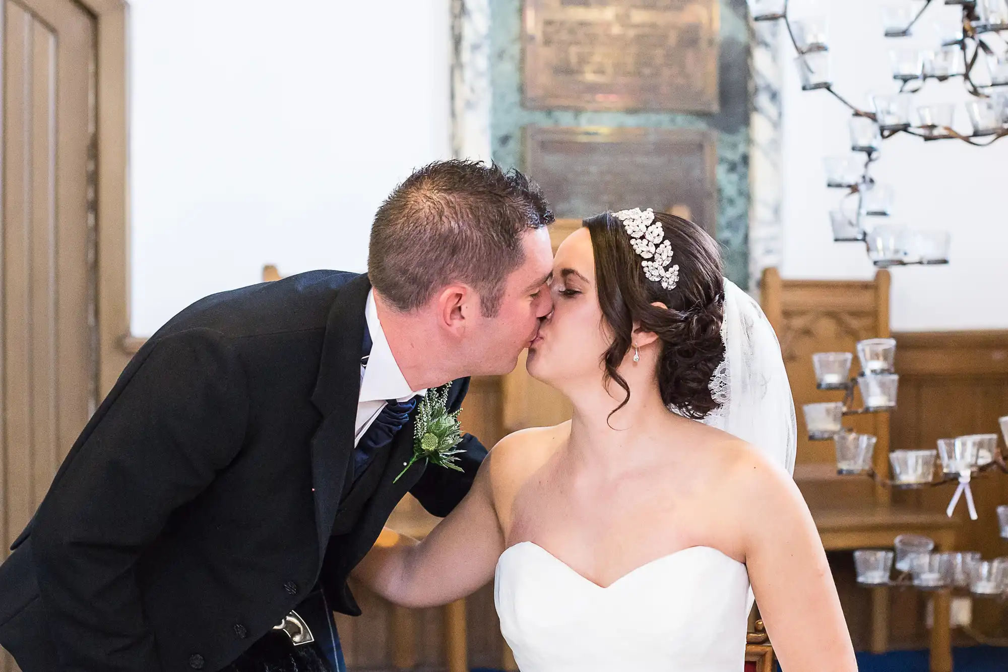 A bride and groom kissing inside a church at their wedding ceremony, with decorative lights in the background.