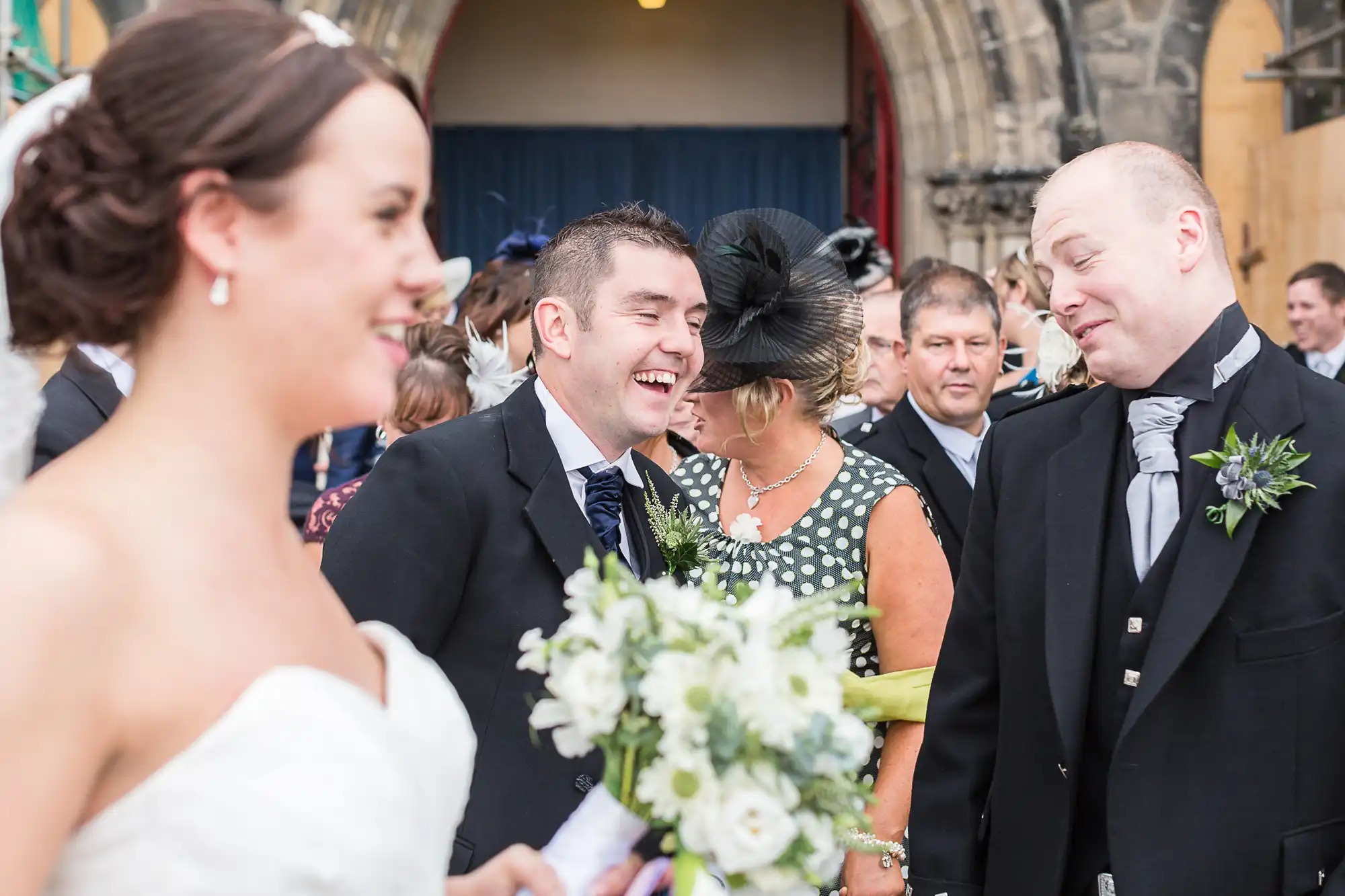 A bride and groom laugh joyously with guests outside a church during their wedding.