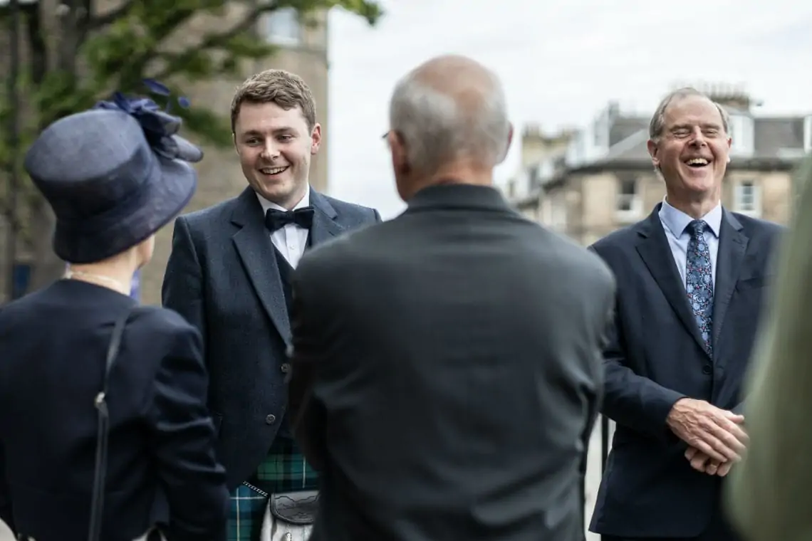 Groom laughing with guests outside church