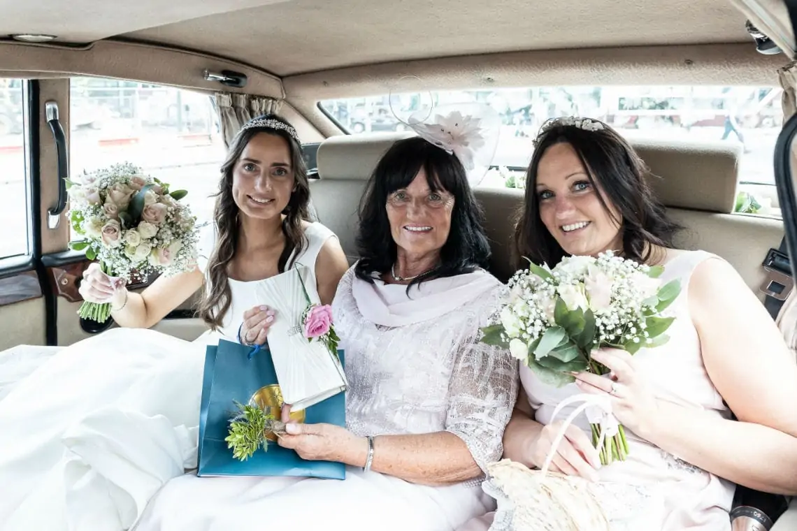 Bride with mother of the bride and bridesmaid in wedding car