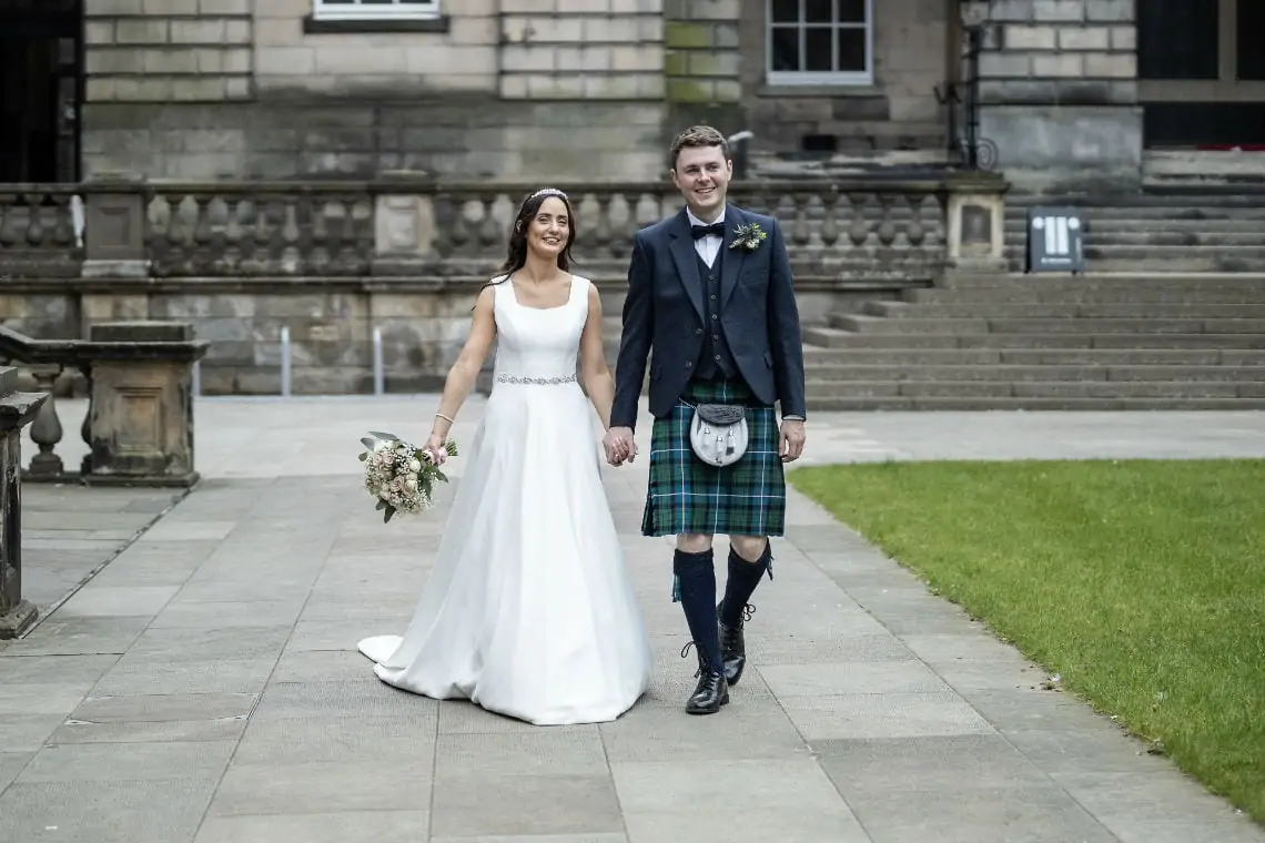 Newlyweds walking towards the camera in the grounds of the Old College