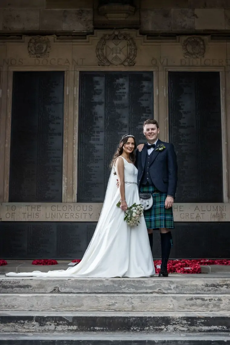 Bride and groom standing in front of a memorial at the college