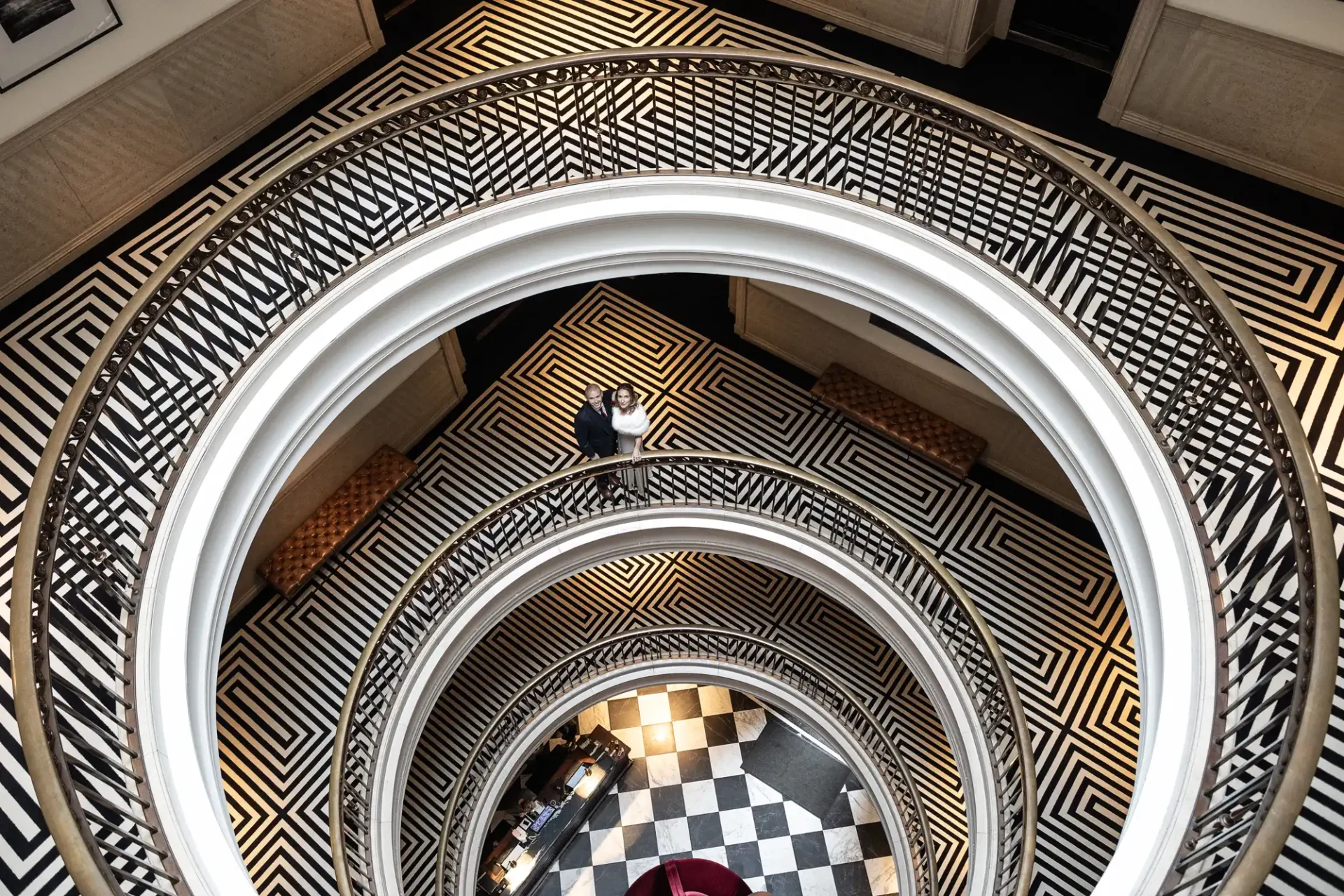 Aerial view inside a multi-level building with spiral staircases, geometric black and white floor patterns, and a person standing on the third level.