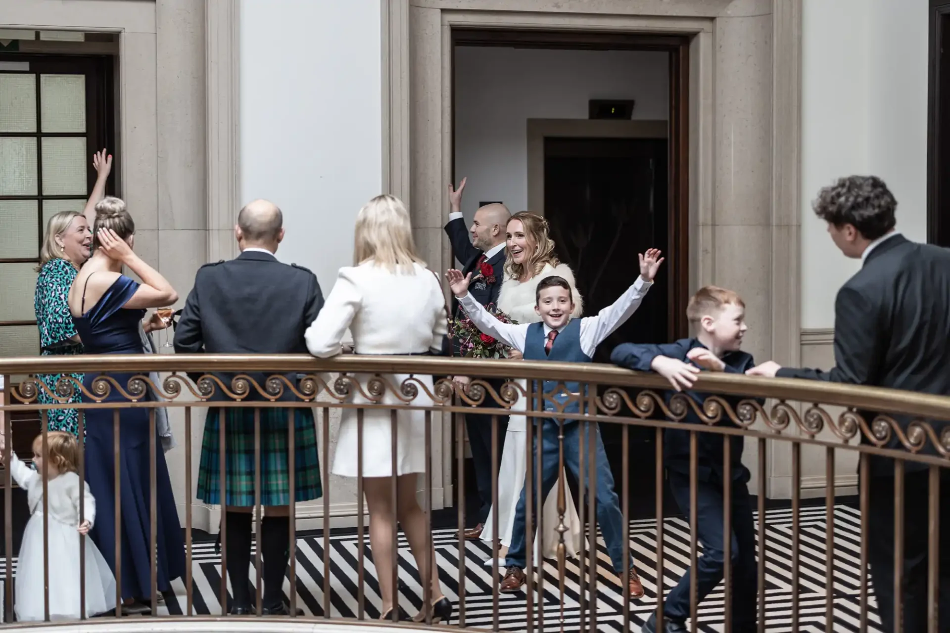 A small group of adults and children celebrate near a railing in a building, with one child raising arms. Black and white striped floor is visible.