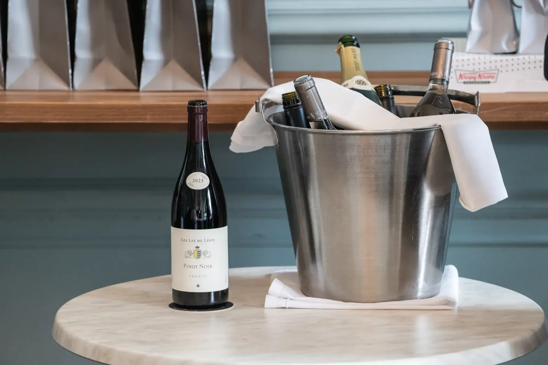 A bottle of red wine stands beside a metal ice bucket filled with chilled white wine bottles on a marble table.