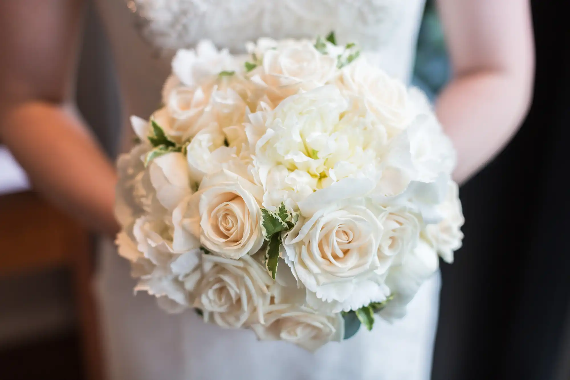 A bride in a lace dress holds a bouquet of white roses and peonies.