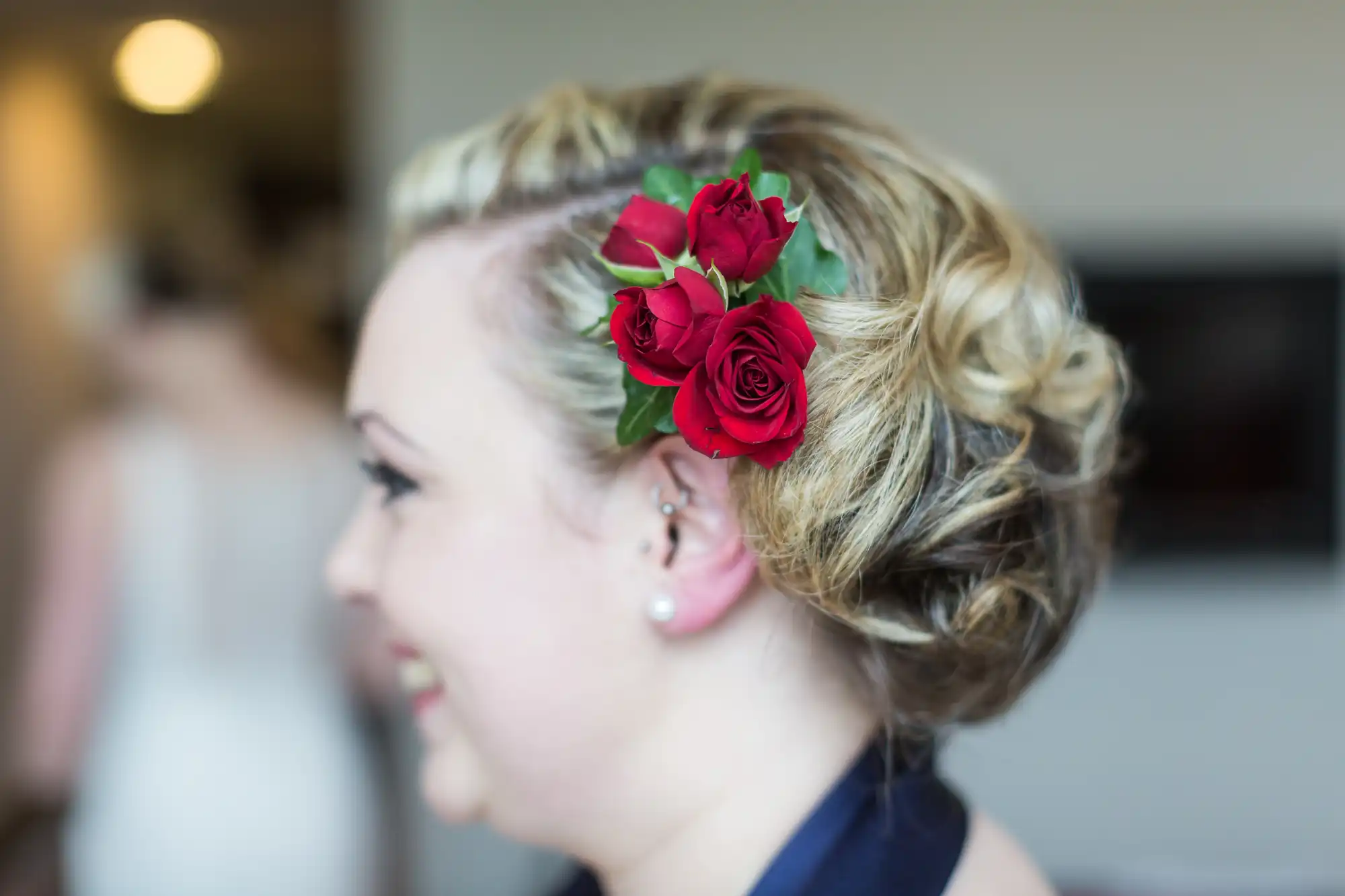 Profile view of a smiling woman with an elegant updo hairstyle adorned with red roses and green leaves.
