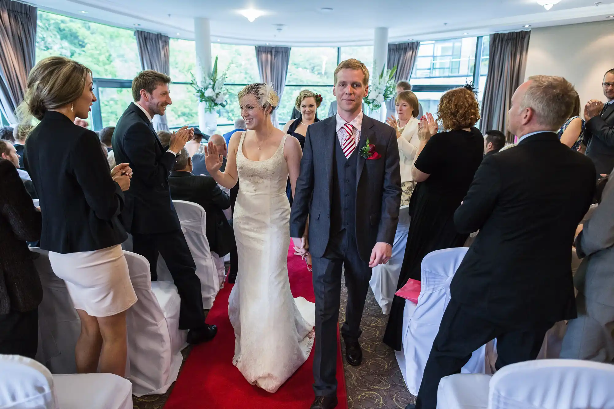 Bride and groom walking down the aisle, surrounded by applauding guests in an indoor wedding venue.