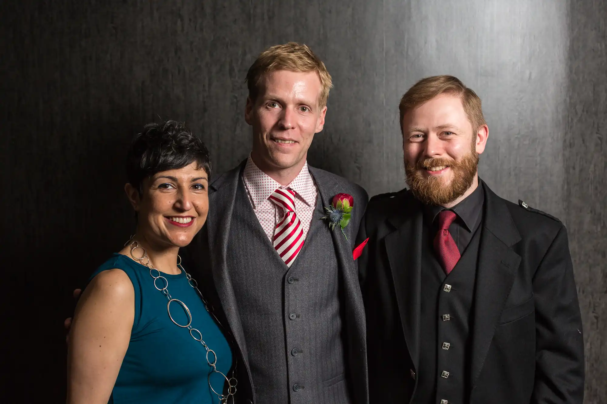 Three adults dressed in formal attire smiling for a photo against a gray textured backdrop.