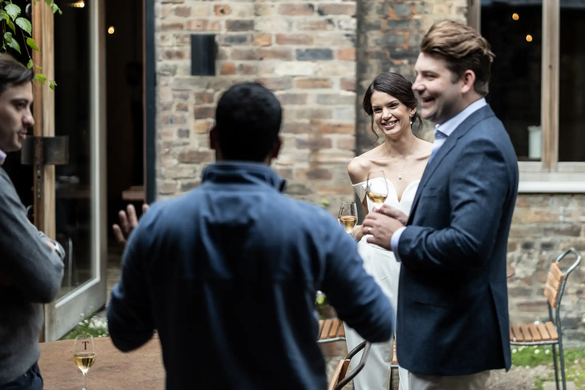 A newlywed couple having a conversation with a guest during their outdoor wedding reception, all smiling and holding drinks.