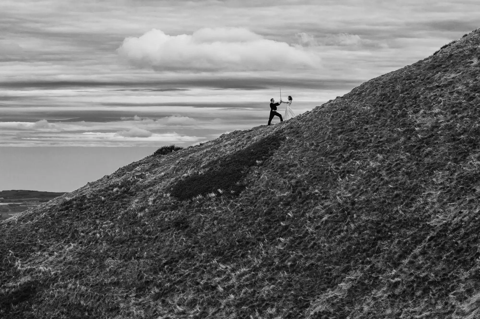 A person hiking up a steep, grassy hill under a cloudy sky, gazing into the distance.