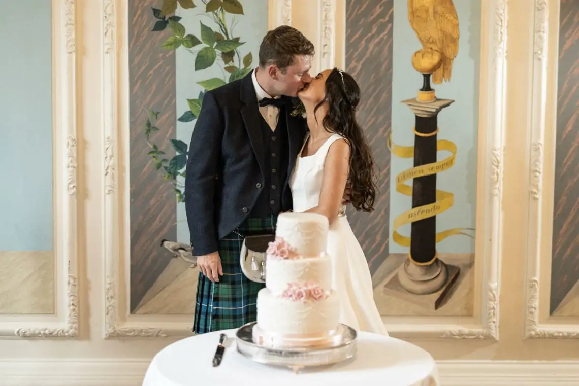 Bride and Groom kiss next to their wedding cake