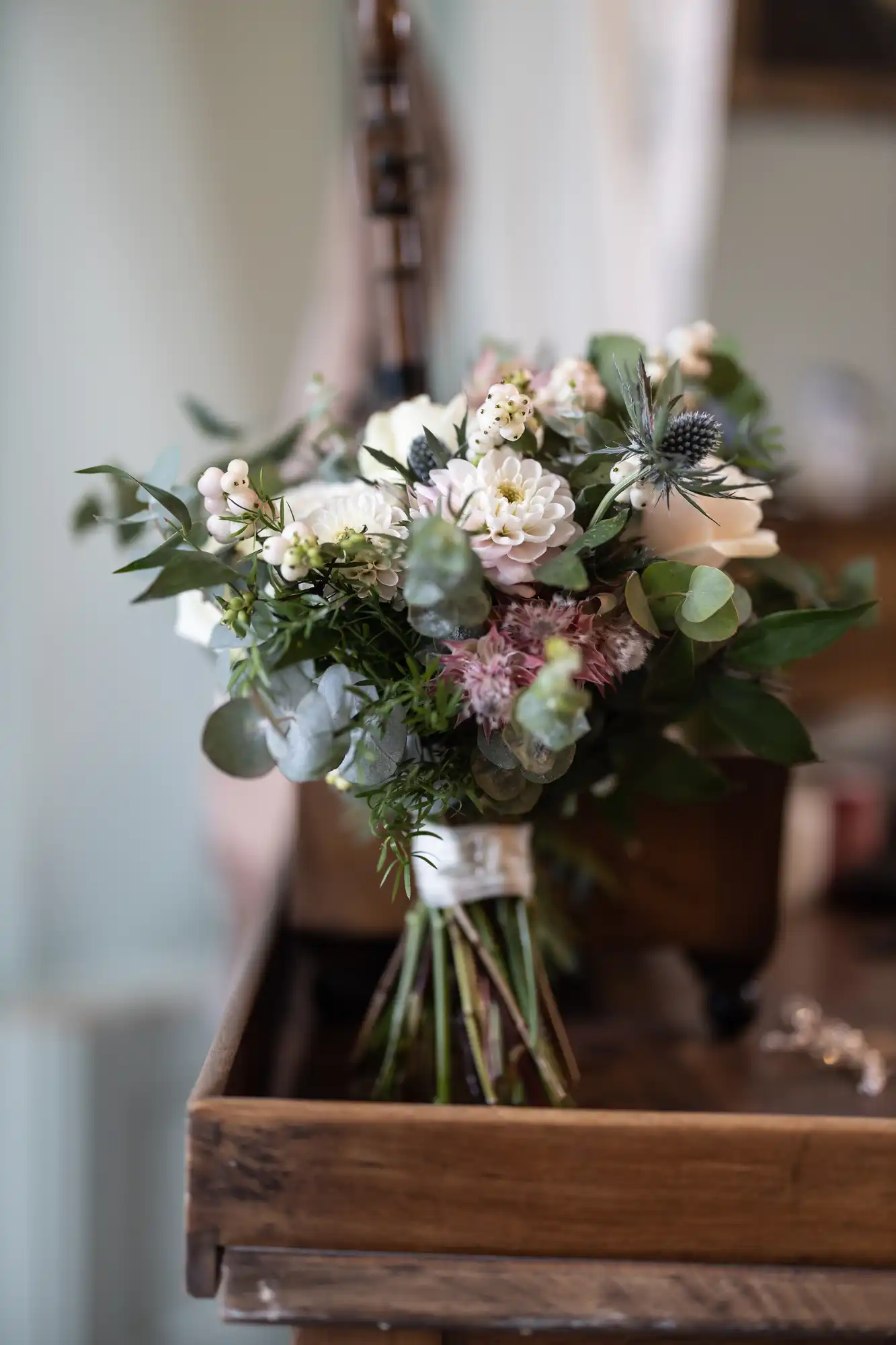 A bouquet of white and pink flowers with green foliage, wrapped at the stems, placed on a wooden surface indoors.