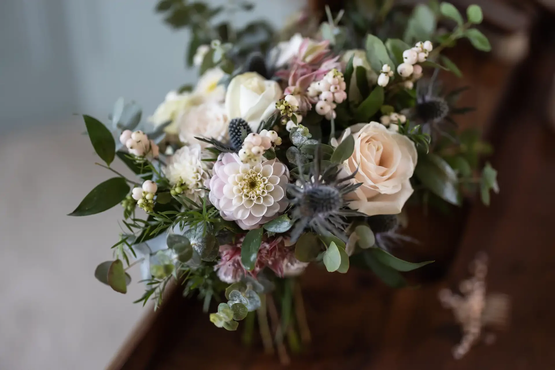 A bouquet of mixed flowers including roses, dahlias, and greenery arranged on a wooden surface.