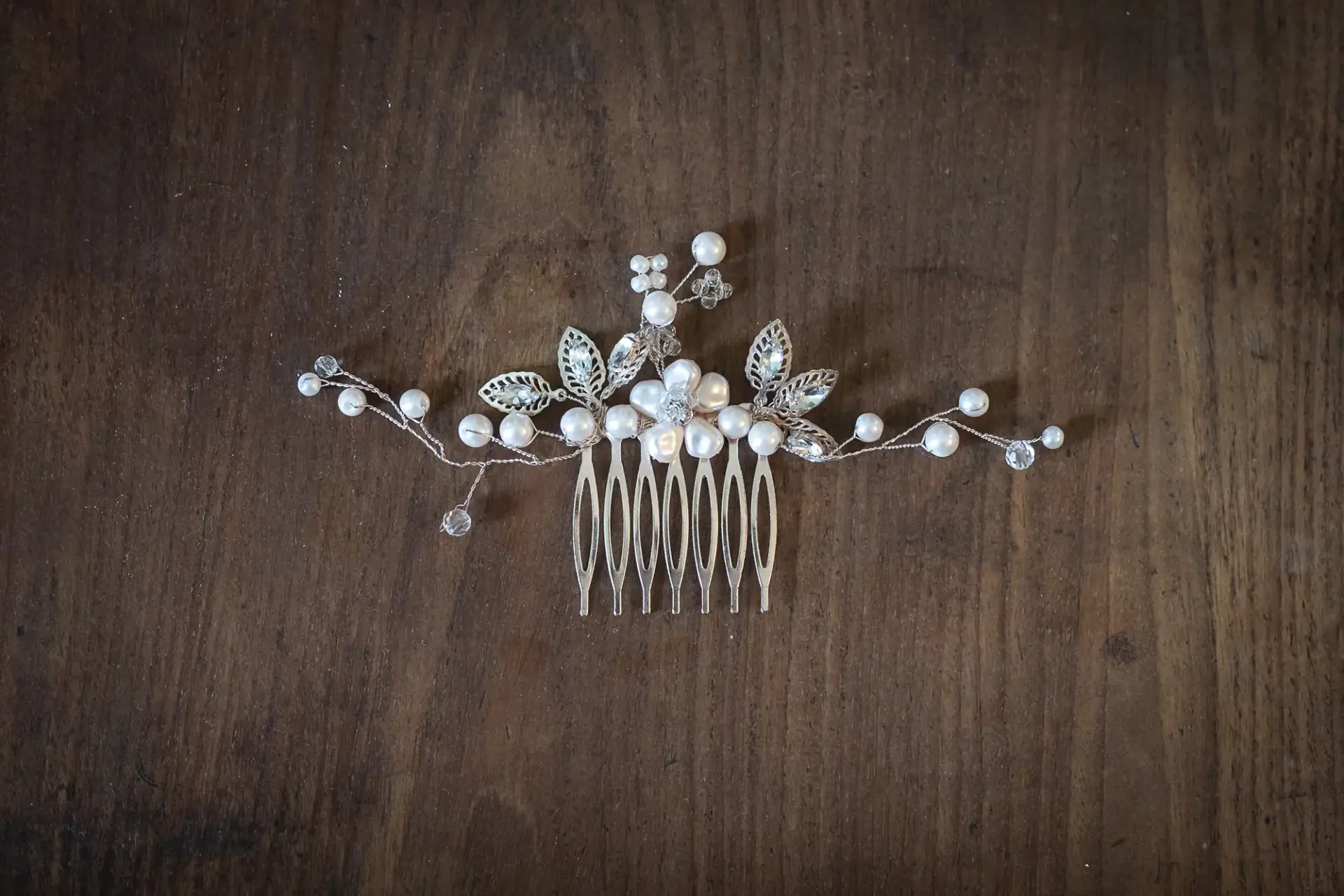 A decorative hair comb with pearls and crystal beads arranged in a floral design, set on a wooden surface.