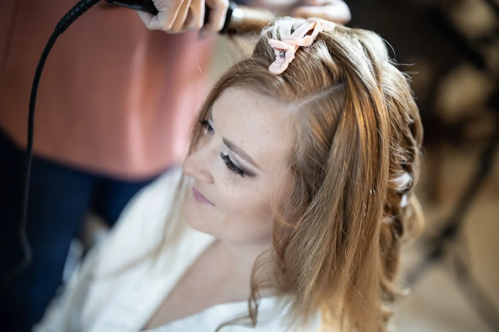 A woman getting her hair styled with a curling iron by another person, with hairpins visible.