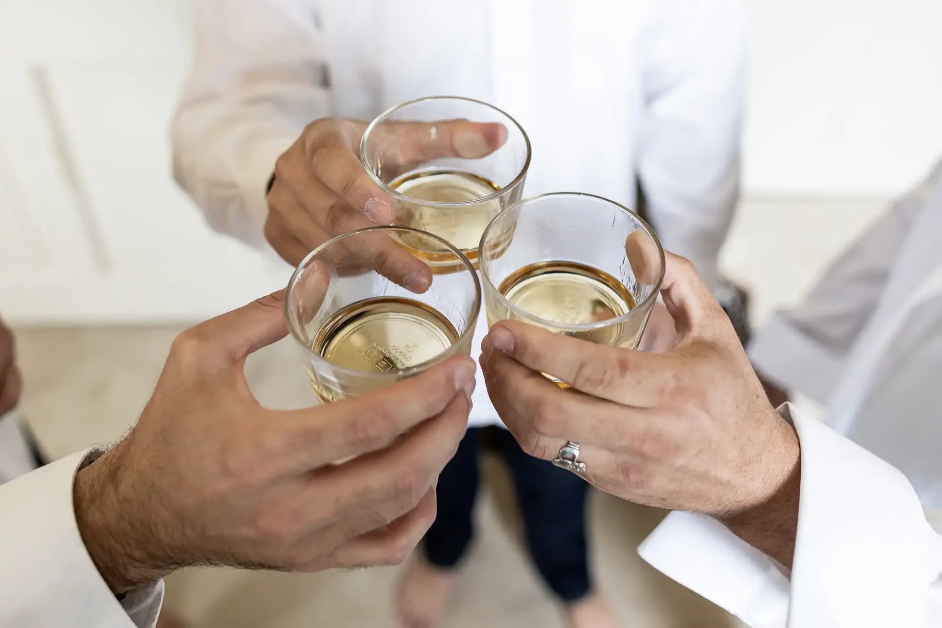 Four people in white shirts clinking glasses filled with a light-colored beverage.