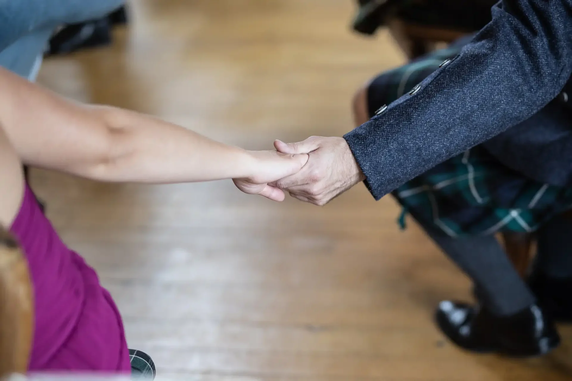 Two people hold hands; one wears a purple top and the other is in a plaid skirt with a grey jacket.