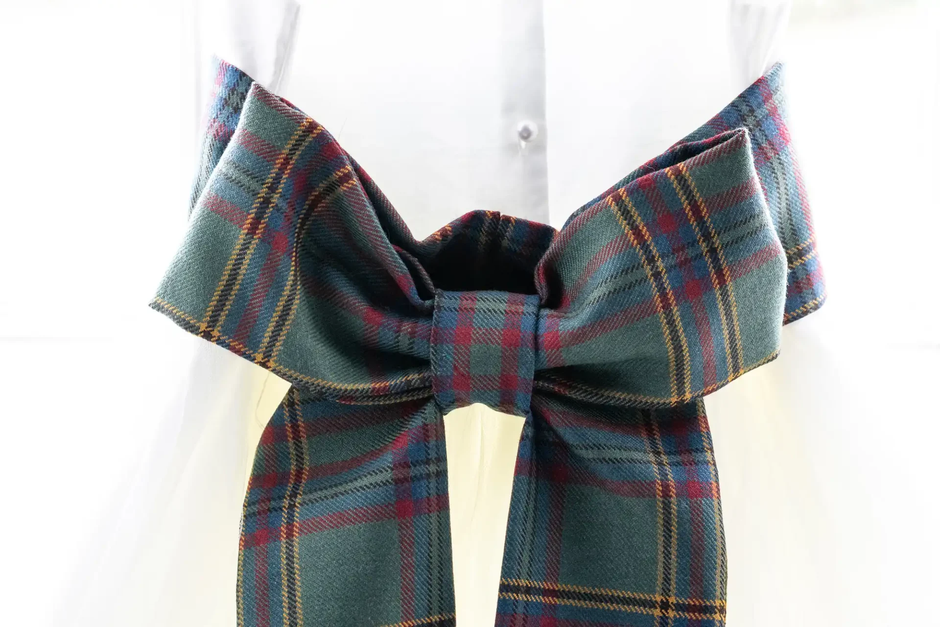 Close-up of a large, plaid bow tied around the waist of a white garment.