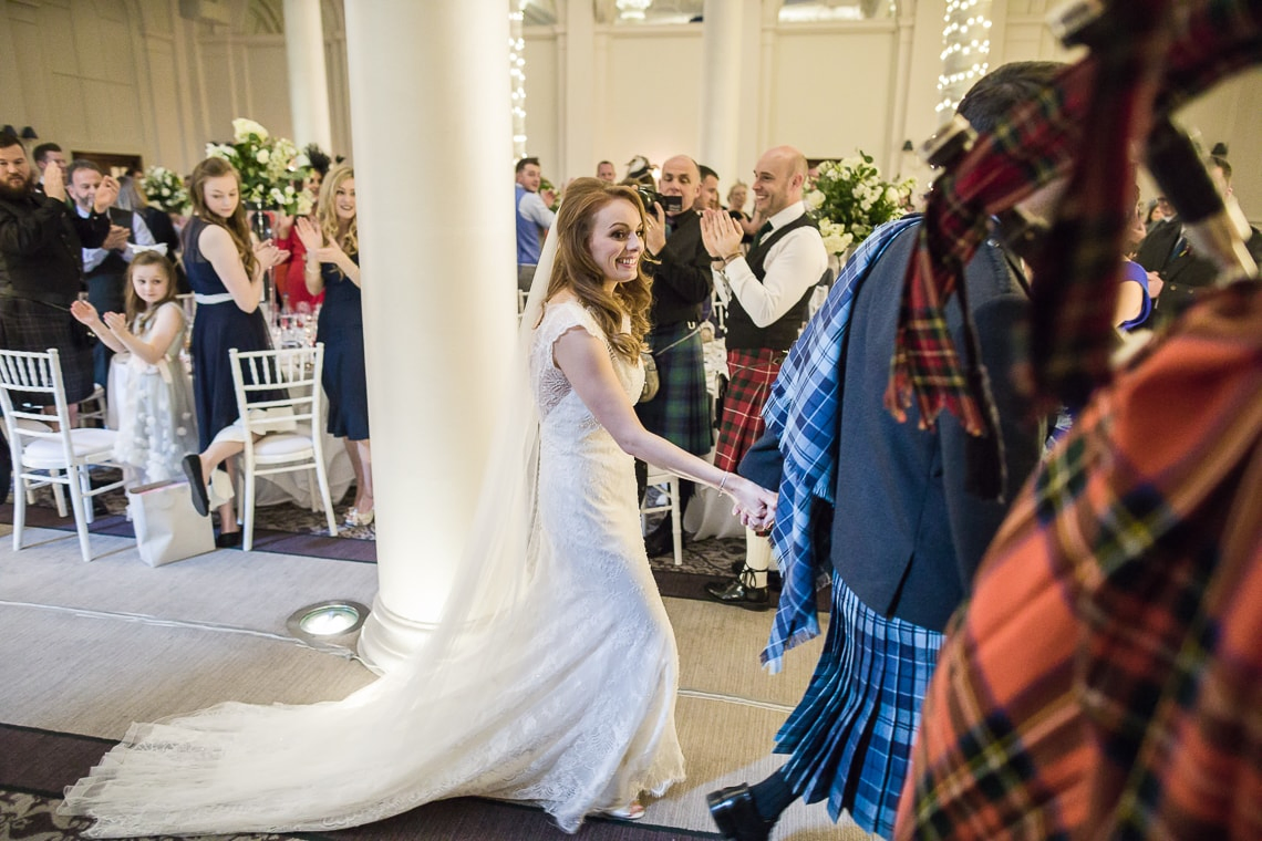 bride and groom are escorted by the piper to the top table