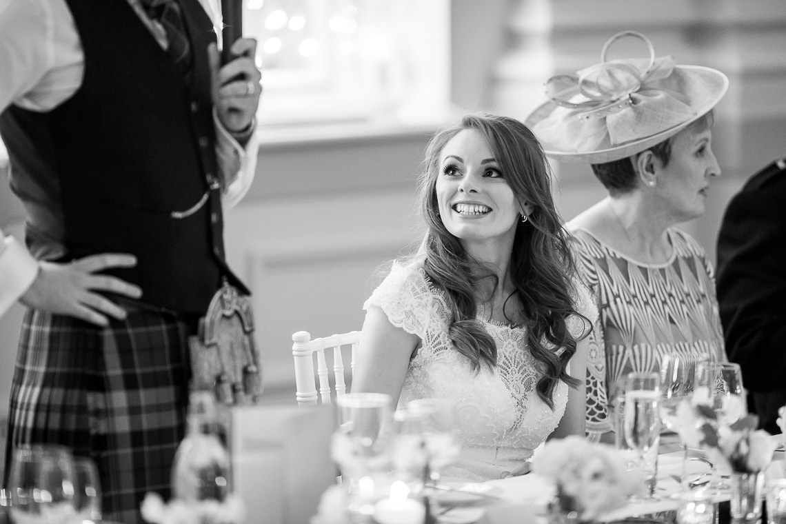 bride smiles during the groom's speech in the King's Hall