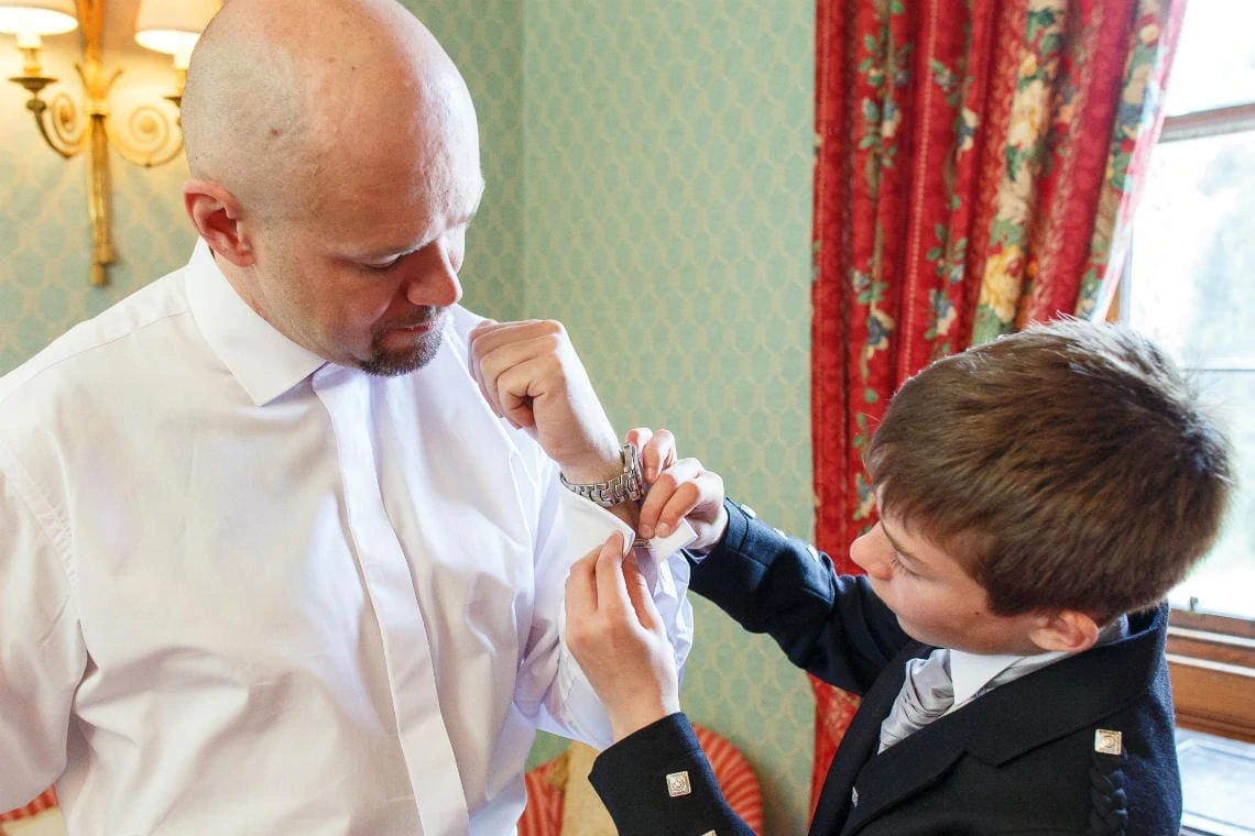 page boy helps groom fit his cufflinks in The Dalwolsey Suite