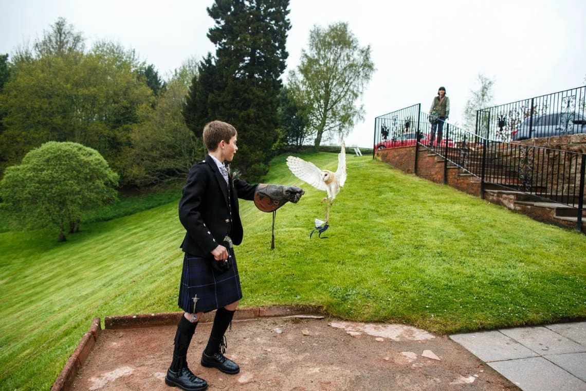 bride's son wearing kilt outfit and leather gauntlet receives owl on the patio