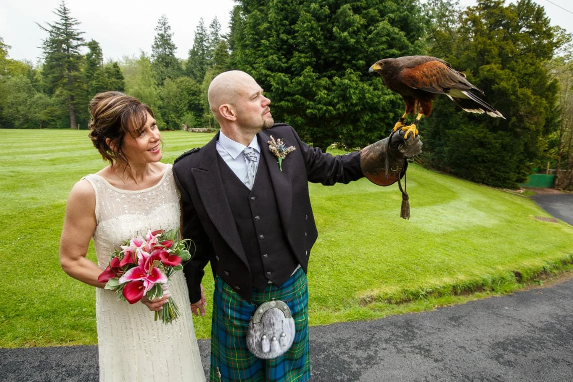 groom holds an eagle on his gauntlet on the castle lawn as bride watches