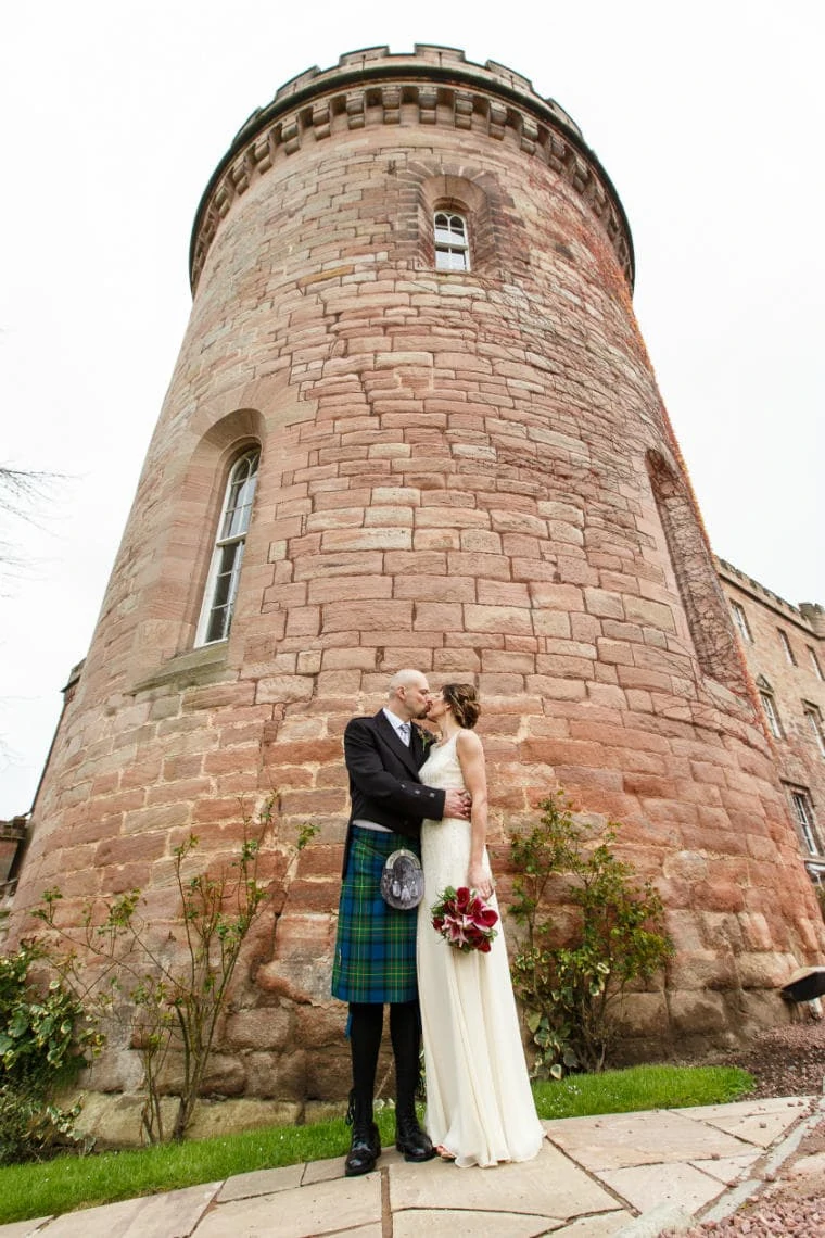 newlyweds kissing in front of the castle tower