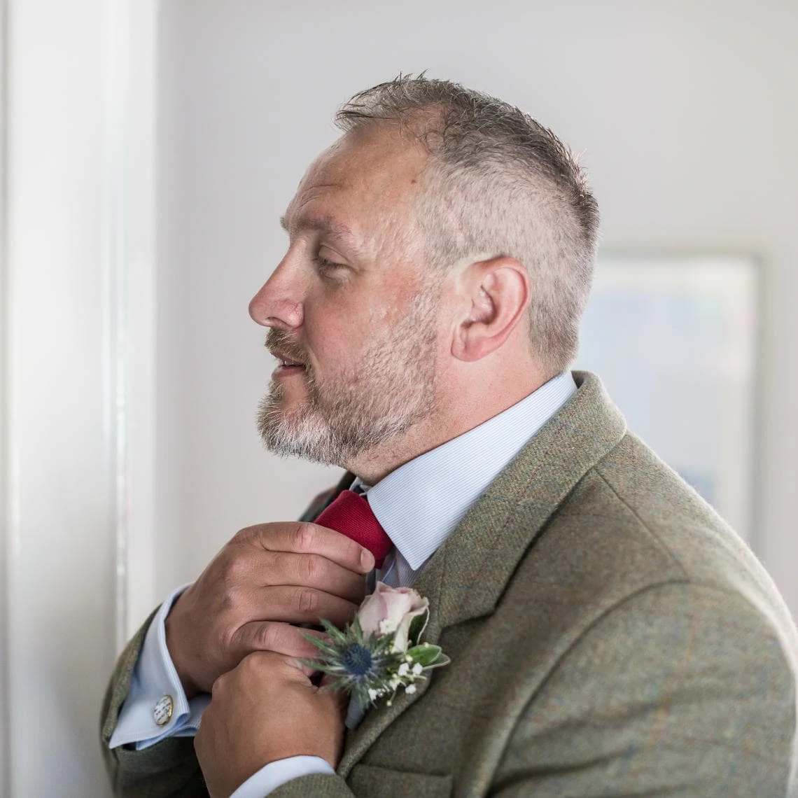 profile of groom sorting his tie in front of mirror