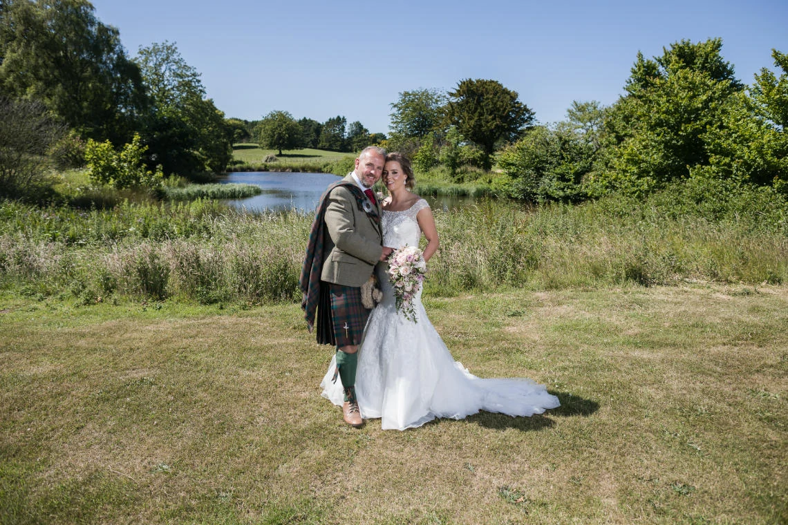 newlyweds in front of pond in the grounds of venue