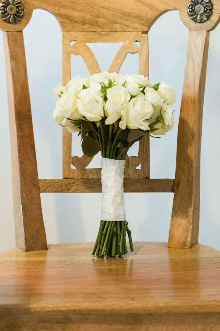 Bridal bouquet of white roses sitting upright against the back of a wooden chair