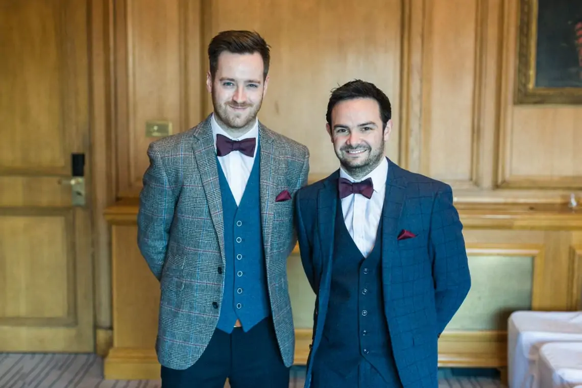 Groomsman and Bestman wearing three-piece suits and bow ties smiling at the camera