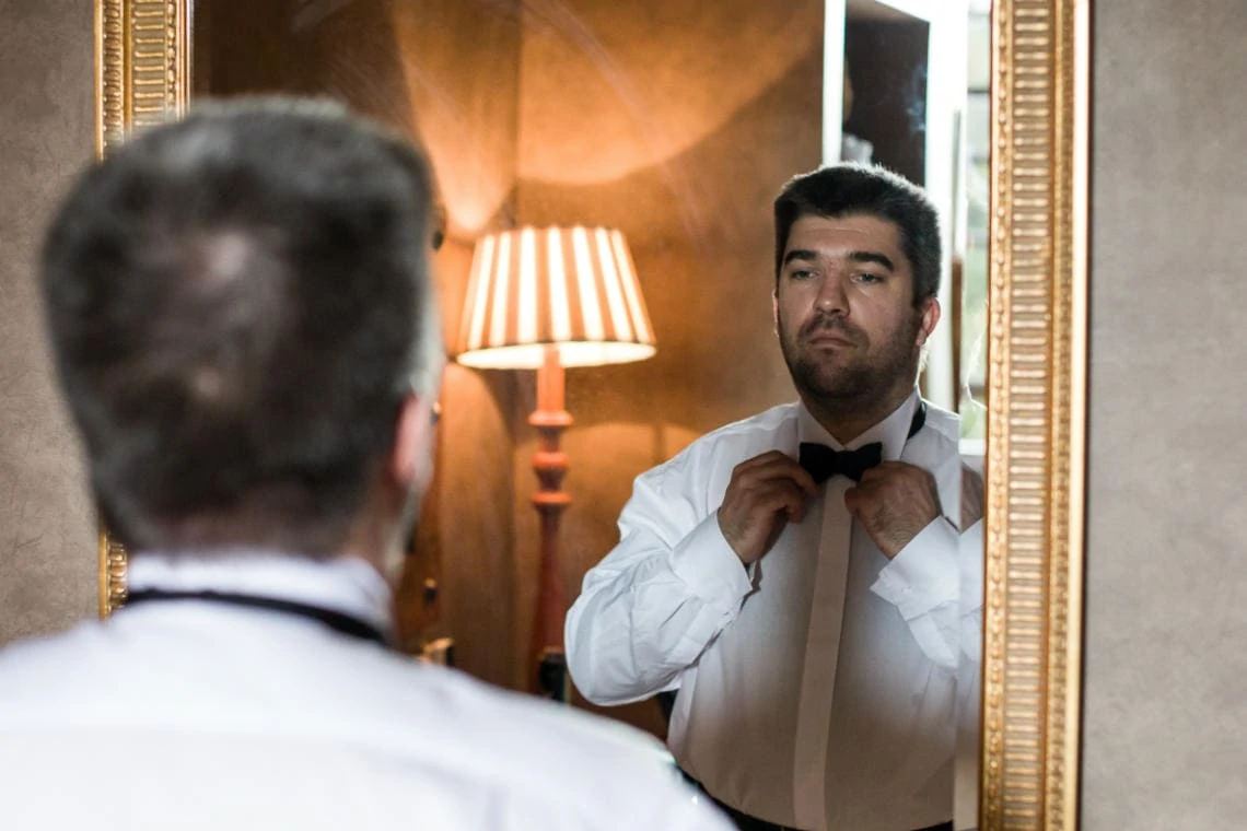photo of groom looking into mirror fixing bow tie