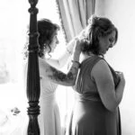 black and white photo of one bridesmaid helping the other bridesmaid put on necklace
