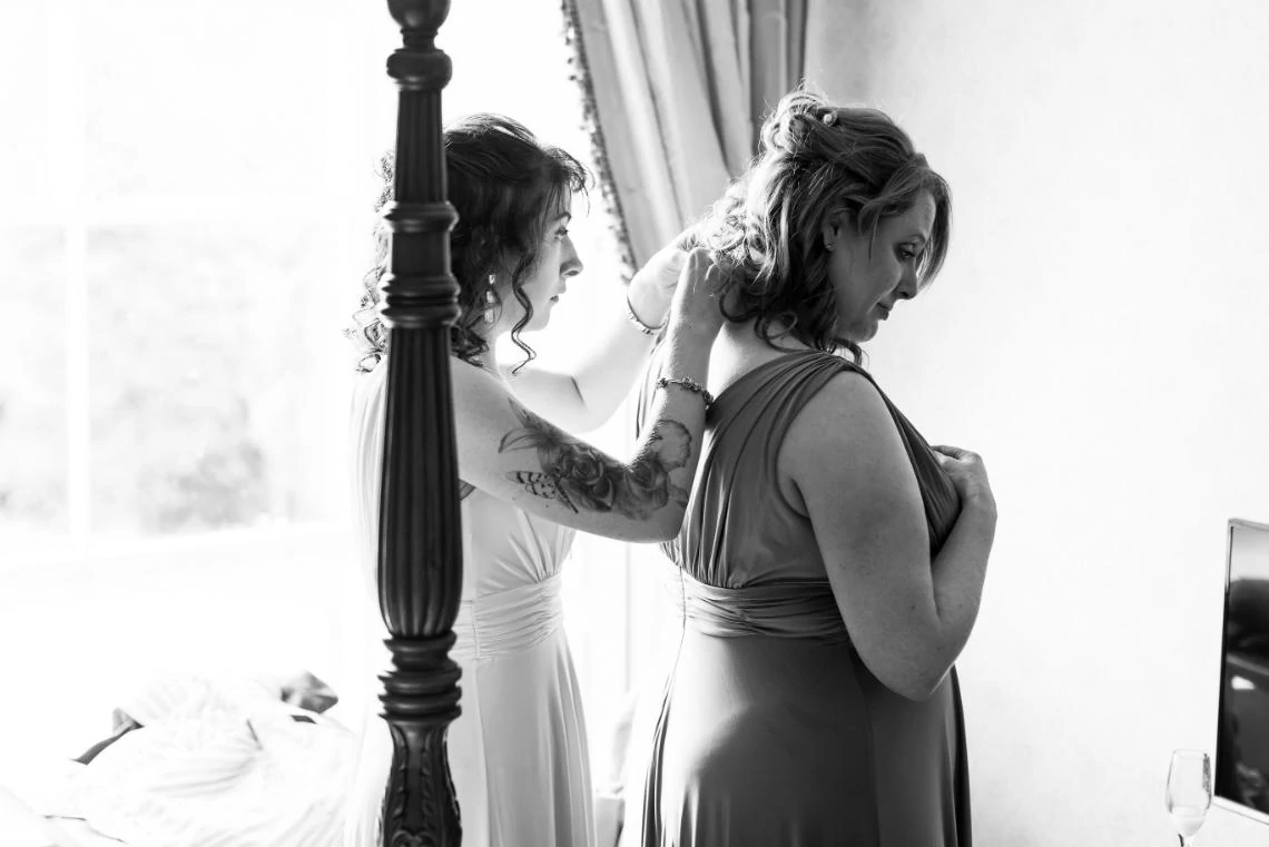 black and white photo of one bridesmaid helping the other bridesmaid put on necklace