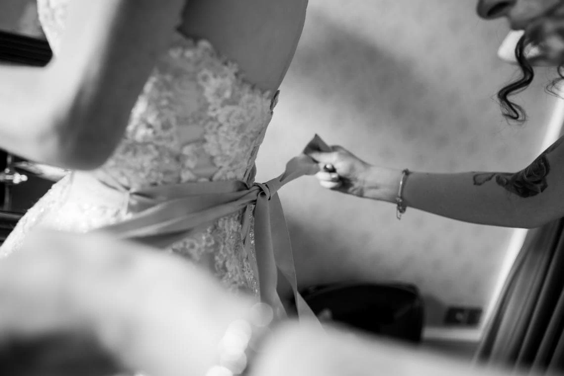 black and white photo of bridesmaid tying the bow on the back of the bride's dress
