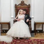 posed photo of bride sitting on groom's knee on thrown