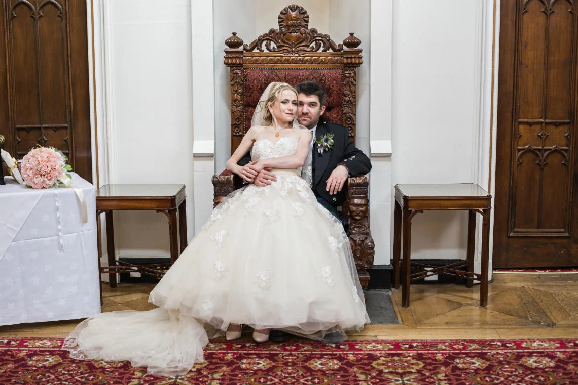 posed photo of bride sitting on groom's knee on thrown