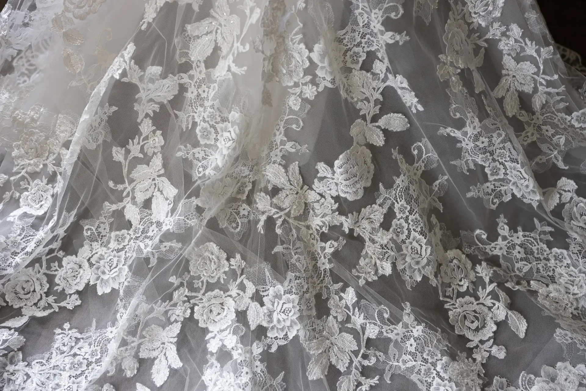 Close-up of delicate white lace fabric with intricate floral embroidery.