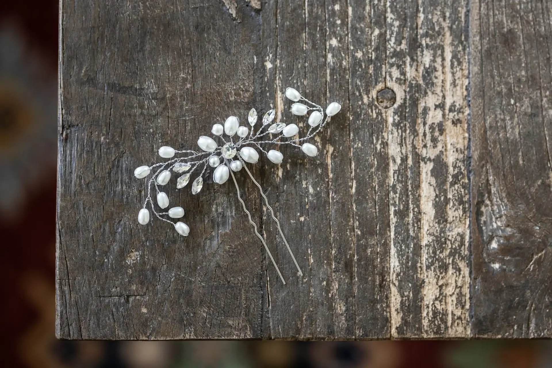 A decorative white floral hairpin resting on a weathered wooden surface.