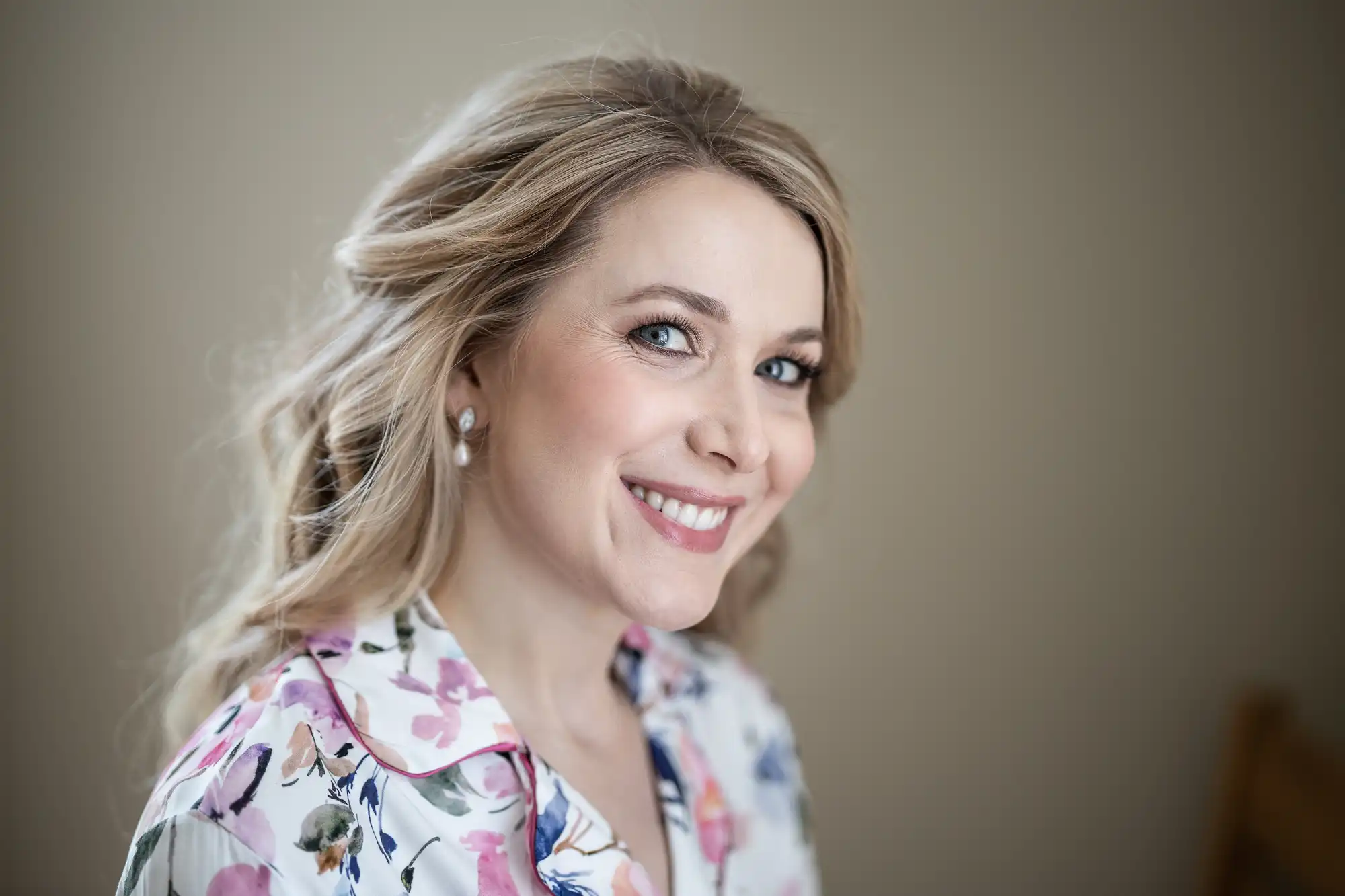 A woman with blonde hair smiling at the camera, wearing a floral blouse. the background is softly blurred.