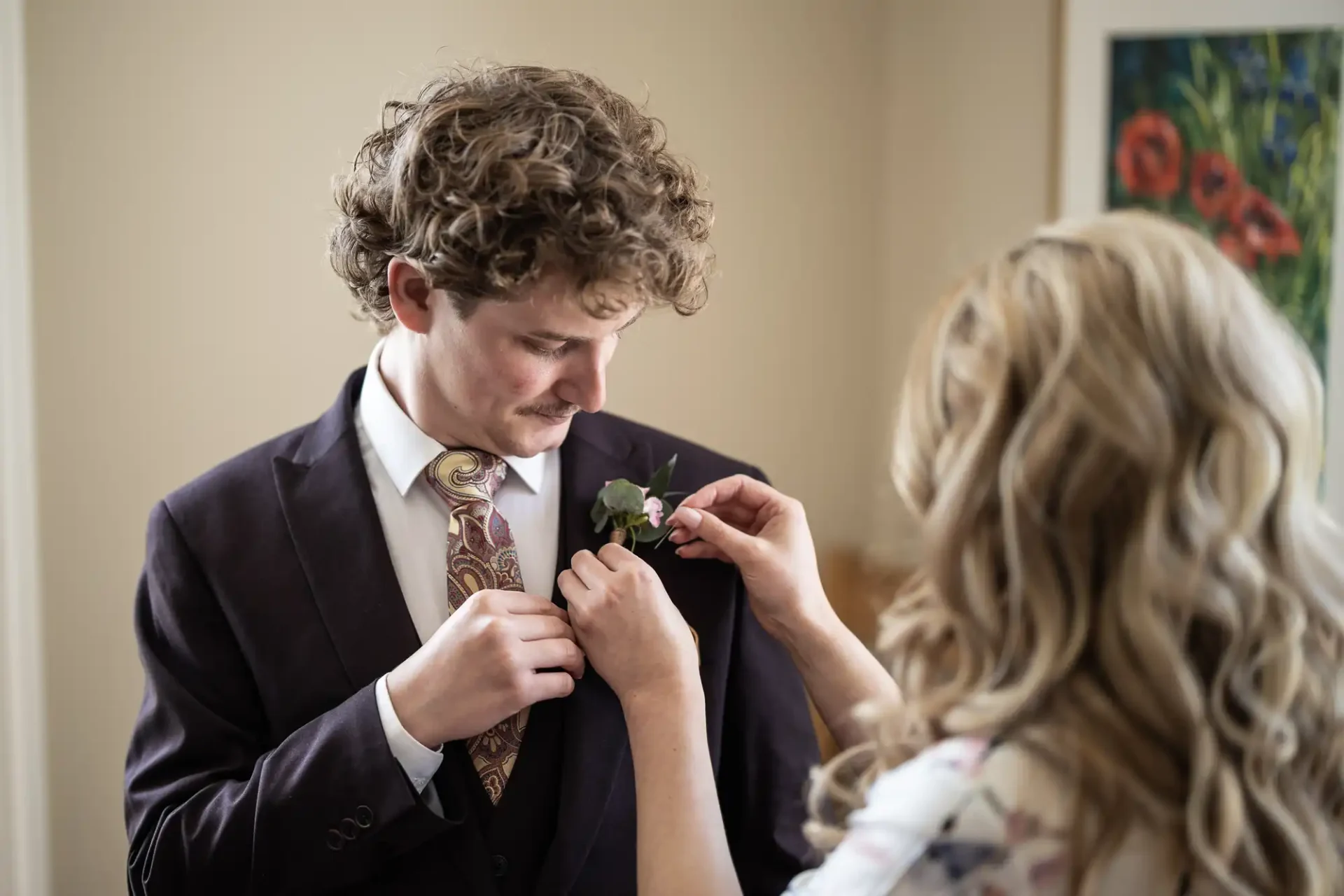 A woman pins a boutonniere on a man's suit lapel as they prepare for a formal event.