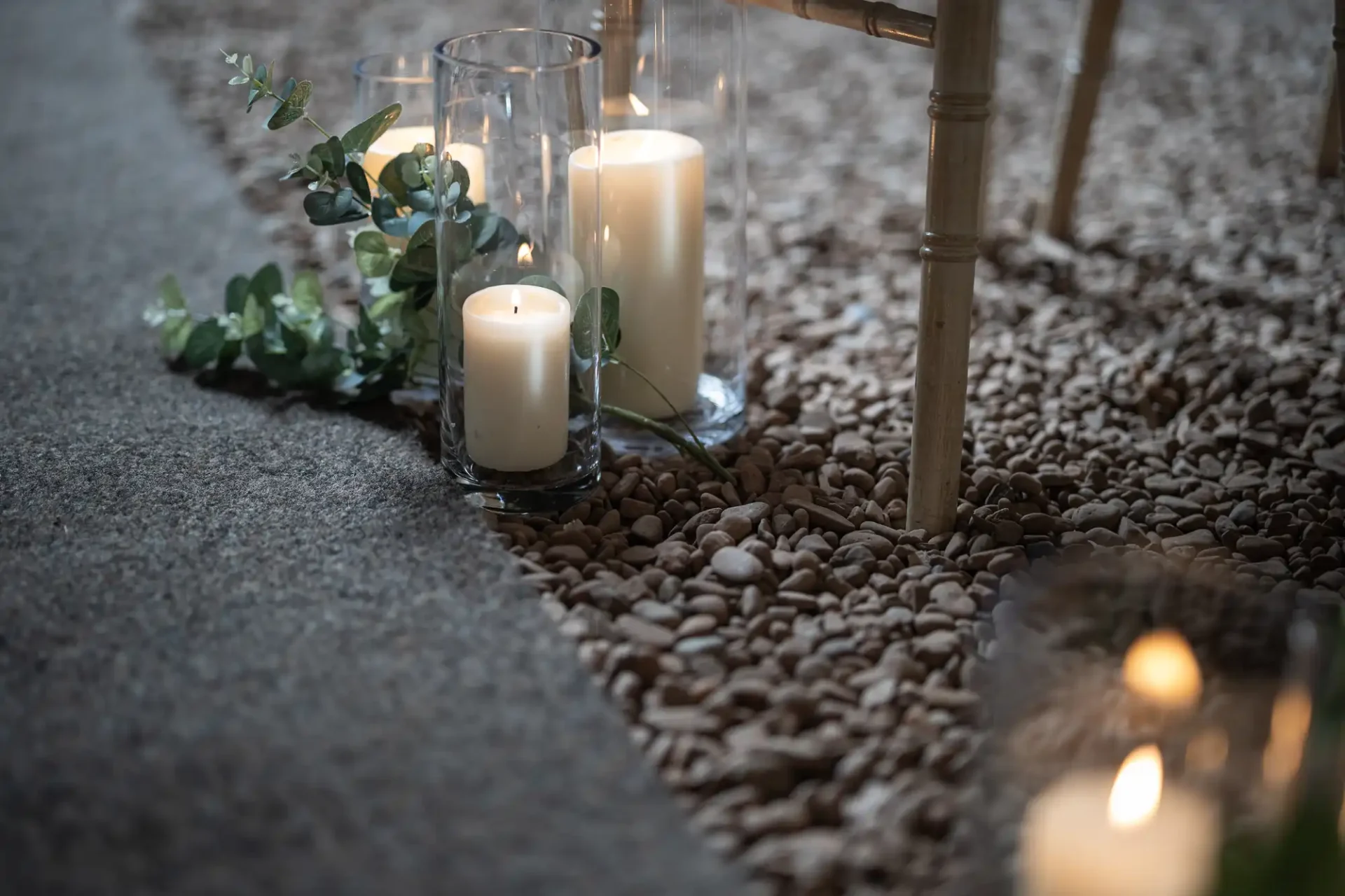 Candles in glass holders and green garlands arranged on a pebble-strewn carpet, creating a serene ambiance.