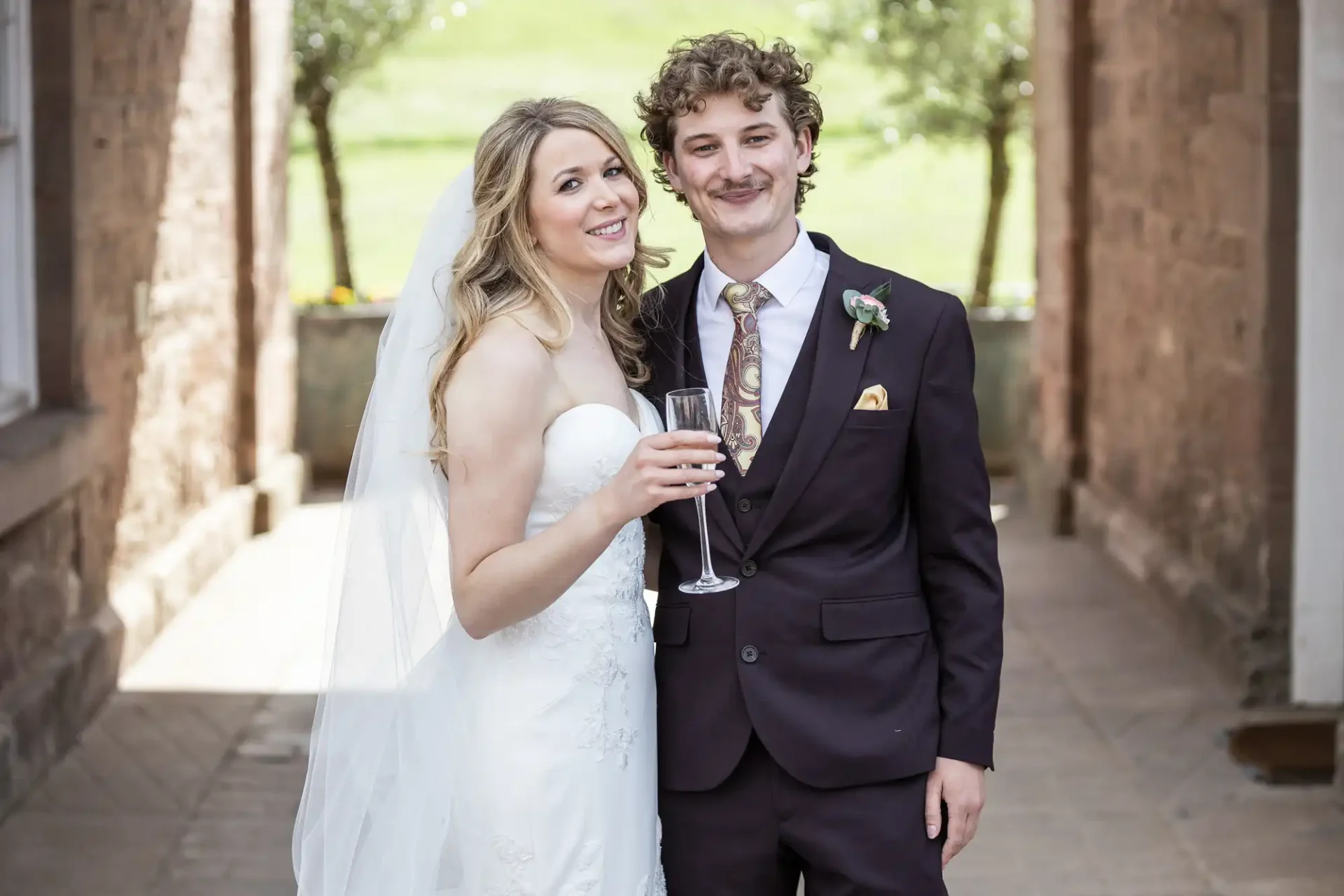 A bride and groom smiling and holding champagne flutes at a wedding venue.