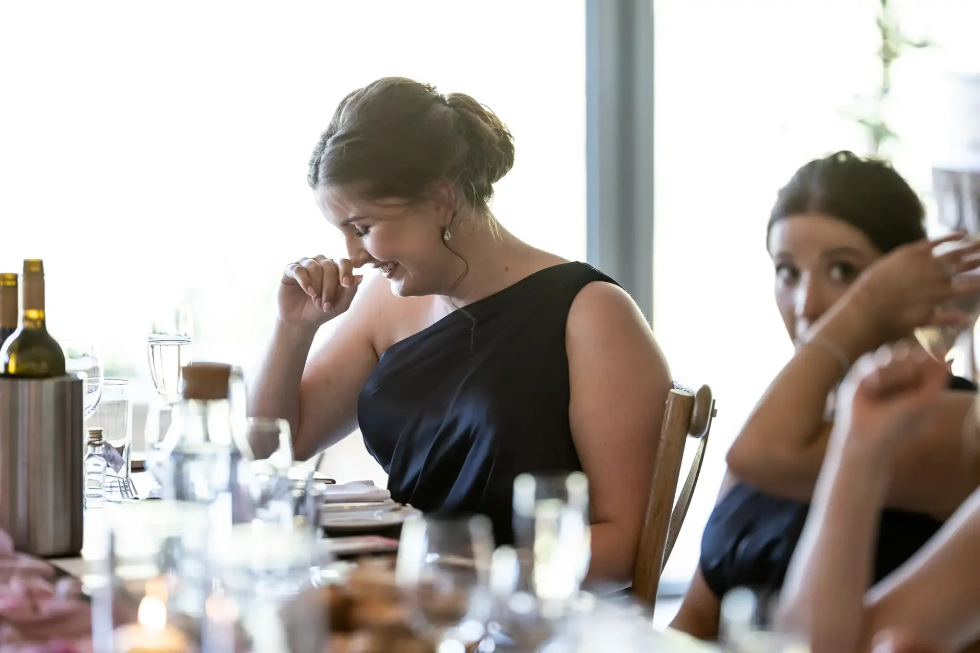 A woman in a black dress seems emotionally moved at a dinner table, with another person looking on.
