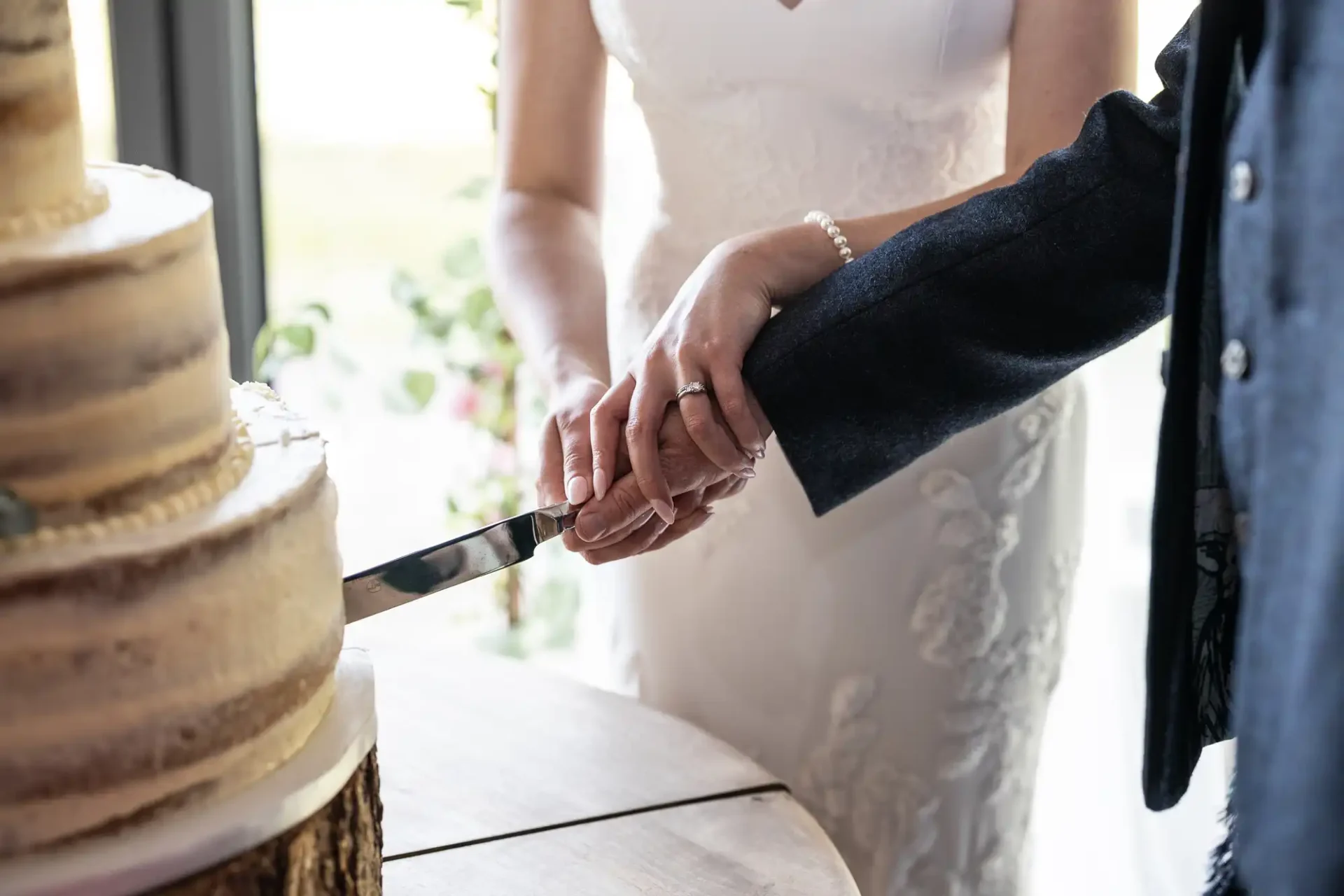 A bride and groom hold hands while cutting a multi-tiered wedding cake.
