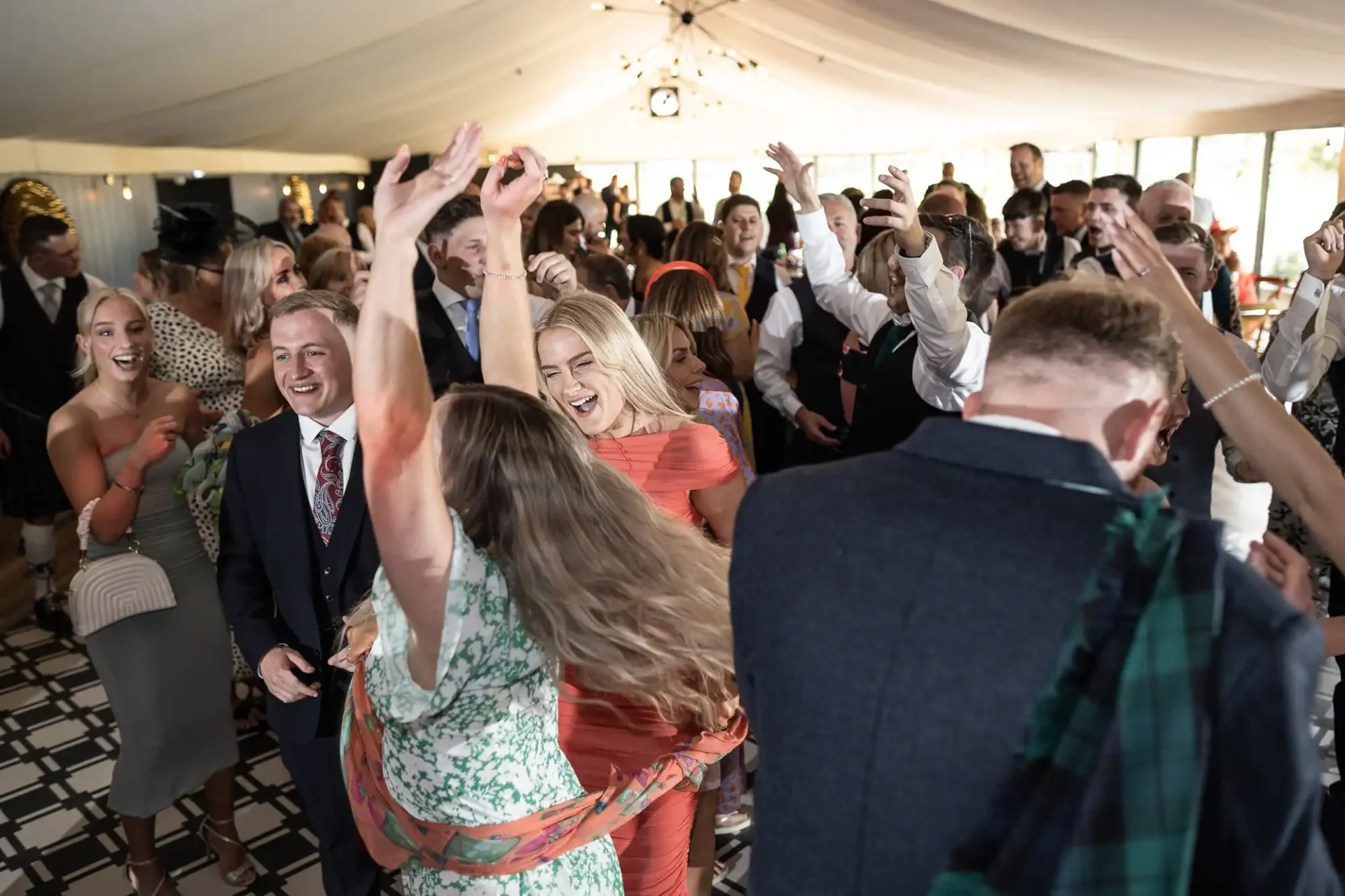Guests joyfully dancing and celebrating at a wedding reception inside a tent.